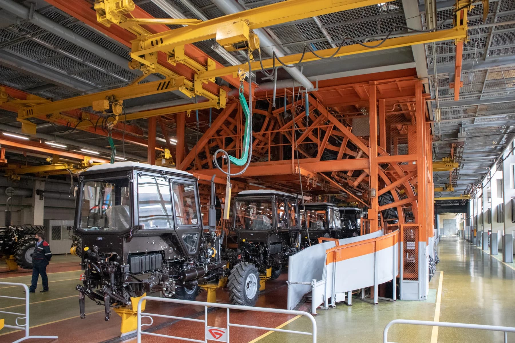 Traktoren an aufeinanderfolgenden Montagestationen unter Hebevorrichtungen in einer Fabrik.